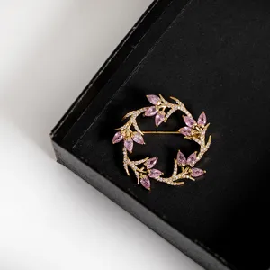 Close-up detail of a circular leaf brooch with pink marquise crystals in a black gift box