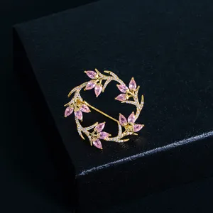 Detailed view of a circular gold-tone leaf brooch with pink gems and micro-pave crystals