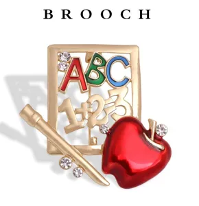 Detailed macro view of teacher-themed gold brooch with ABC letters and red apple decoration