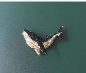 Detailed view of an elegant whale brooch with black and white rhinestones on a green surface