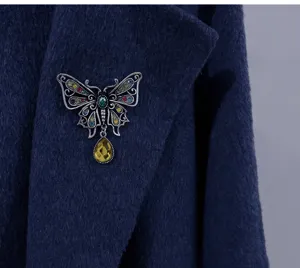 Close-up of a vintage hollow butterfly brooch with a yellow waterdrop pendant on a coat.