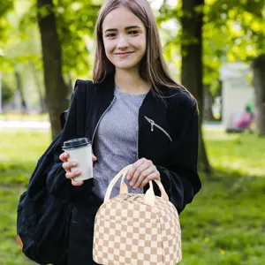 Young woman holding a checkered corduroy insulated lunch bag in a lush sunny park