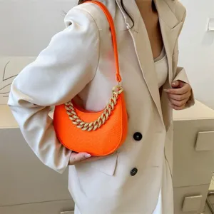 Detalle del bolso de fieltro naranja con cadena dorada gruesa lucido por una modelo.