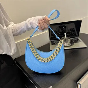 Detalle de un bolso de hombro de fieltro azul con una elegante cadena dorada gruesa.