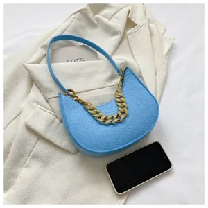 Detalle de bolso hobo azul textura cocodrilo con cadena dorada sobre fondo de chaqueta