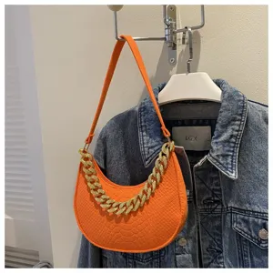 Bolso de hombro media luna de fieltro naranja con cadena dorada sobre fondo de mezclilla