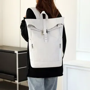 Back view of a casual light grey roll-top backpack worn by a model in an urban setting