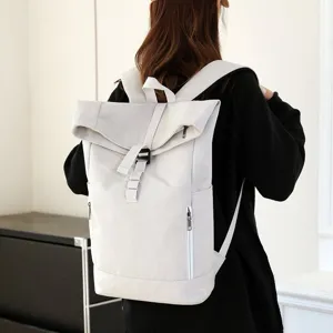 Close-up detail of a minimalist beige roll-top backpack being worn in an urban environment.