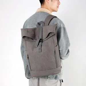 A man wearing a grey urban leisure canvas backpack with roll-top design in a studio