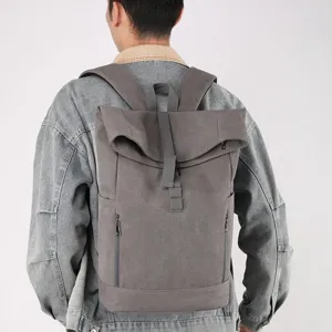 Detailed view of gray canvas roll-top backpack with magnetic buckle worn on person