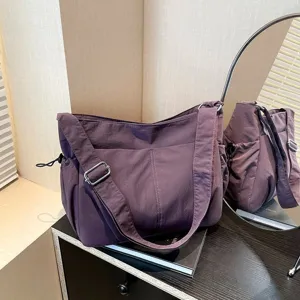 Vista ravvicinata della borsa a tracolla in nylon viola con cerniera e cinghia regolabile.
