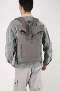 Back view of the grey roll-top laptop backpack worn by a model in a casual outfit.