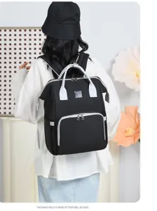 Back view of a premium black mummy backpack with gray handles being worn by a model