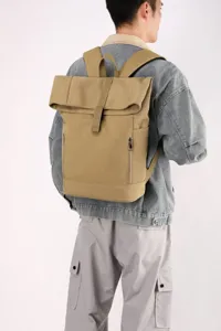 Back view of a khaki urban casual canvas backpack worn by a model in a denim jacket