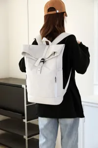 Detailed view of a white minimalist roll-top backpack worn by a model in an urban setting