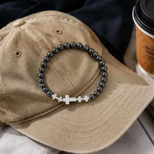 Primer plano de pulsera de cuentas de hematita con cruces de plata en gorra.