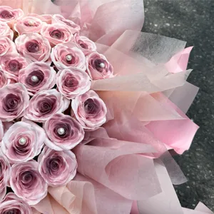 Nahaufnahme des rosa kuenstlichen Rosenstrausses mit Perlenmitte und feiner Verpackung.