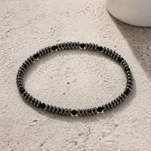 Primo piano di una collana di perline di ematite e pietre nere sfaccettate sulla sabbia.