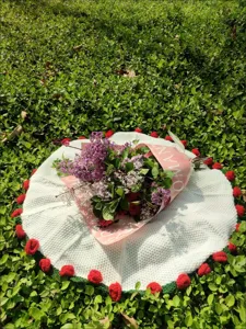Handmade white knitted circular blanket with red pom-poms and flower bouquet gift detail