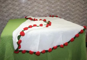Handmade knitted white blanket detail featuring red roses and green leaves, cozy home decor item.