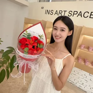 Detail view of a model holding a vibrant red soap flower bouquet with roses and lilies