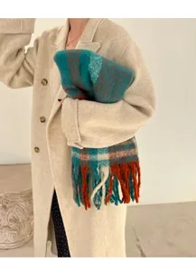 Close-up of thick colorful plaid mohair scarf with tassels held by a model in winter coat