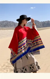 Red and beige ethnic geometric poncho with tassels, shown in a desert travel setting.