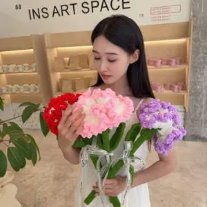 Detail of a handmade knitted carnation bouquet held by a model in a cozy cafe setting.