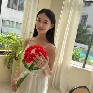 Asian woman holding a beautiful handmade red crochet carnation in a bright sunlit room