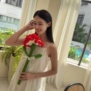 Close-up of a handmade red and white crocheted carnation flower held by an Asian model