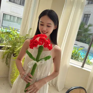 Handmade red crochet carnation flower held by a smiling woman in a bright indoor room