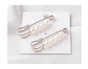 Detailed view of two elegant silver safety pin brooches with white pearls on a display card