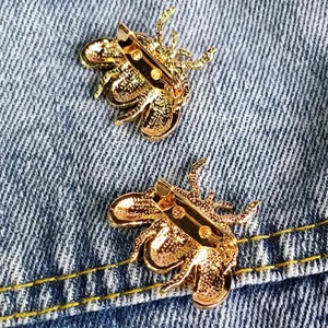 Detailed view of two gold-toned beetle brooches with safety pins on blue denim fabric