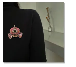 Detail van een roze strass pompoenkoets broche gespeld op een zwarte coltrui voor dames.