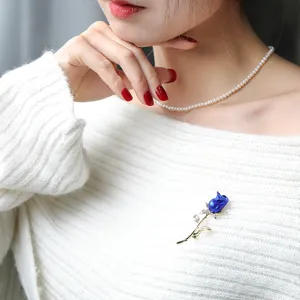 Detailansicht einer eleganten blauen Rosenbrosche an einem weißen Strickpullover für Damen