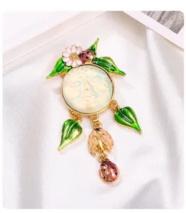Gros plan d'une broche en émail vintage avec visage de lune et glands de coccinelle