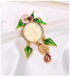 Détail d'une broche émaillée vintage avec un visage sculpté et des pendentifs coccinelles