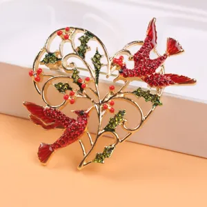 Macro view of golden heart brooch featuring red birds and green holly leaf details