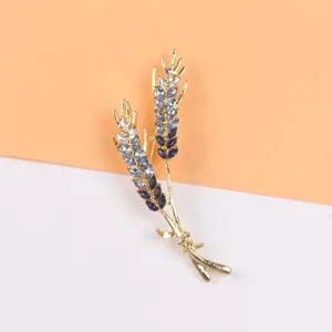 Detailopname van een elegante goudkleurige tarwe-aar broche met blauwe verloopkristallen.