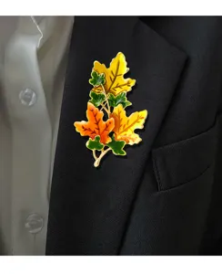 Close-up detail of an elegant enamel maple leaf brooch pinned to a black suit lapel.