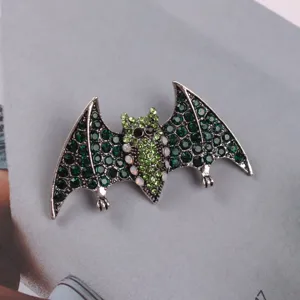 Close-up of a sparkling green rhinestone bat brooch on a gray magazine page background