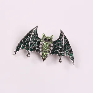 Close-up of a creative alloy bat brooch featuring vibrant green rhinestones and opal accents.