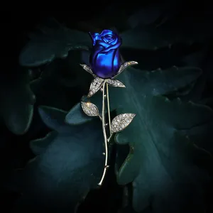 Detailansicht einer blauen Rosenbrosche mit goldenem Stiel und Kristallen auf Blättern
