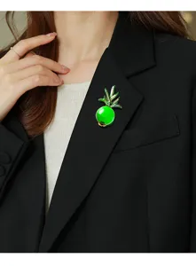 Detail shot of vibrant green pineapple brooch worn on a classic black blazer lapel.