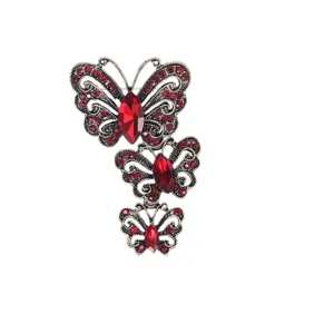 Elegante broche vintage con tres mariposas y cristales rojos sobre fondo blanco.