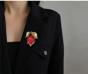 Detalle de un broche de fresa de resina roja con hojas doradas en un blazer negro