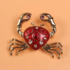 Detailed view of a gold-toned crab brooch with red enamel and sparkling rhinestones.