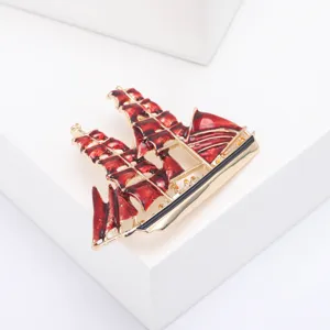 Gedetailleerd overzicht van een vintage zeilbootbroche met rode emaille zeilen en goud