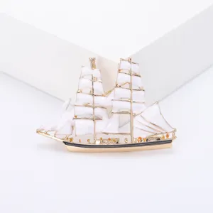 Detailopname van een vergulde zeilbootbroche met elegante witte geëmailleerde zeilen