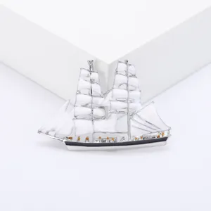 Gedetailleerde macrofoto van een elegante zilveren zeilschipbroche met witte zeilen.